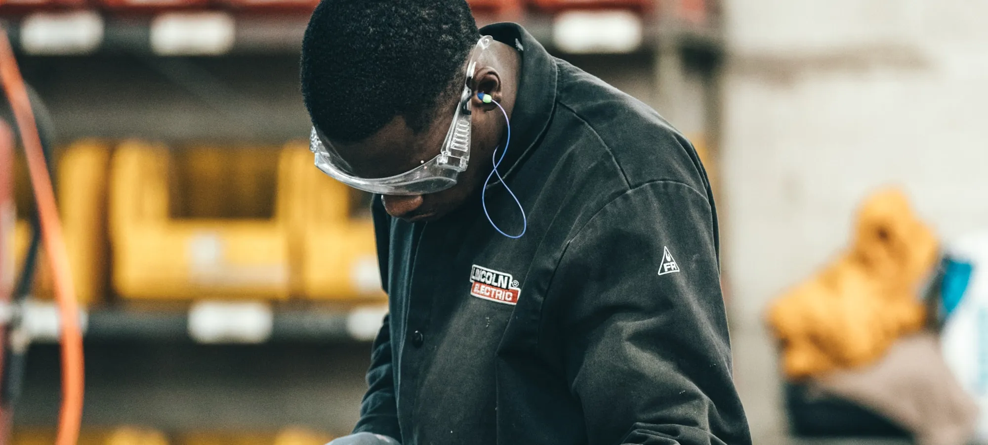 Industrial worker handling metal components in a manufacturing facility.